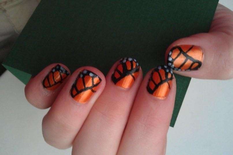 Nail art arancione con ali di farfalla nere